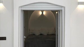 A doorway leading to a bedroom with a bed, a nightstand, and a wall-mounted light fixture. - - IMI White house 2 - (Imi Ouaddar)
