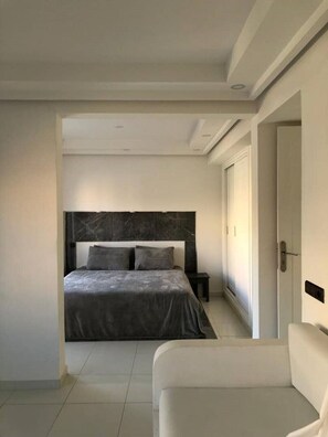 A modern bedroom with a large bed, a bedside table, and a white sofa. - - IMI White house 2 - (Imi Ouaddar)