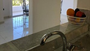 Una cocina moderna con un lavamanos de acero inoxidable, una cesta de frutas en la encimera y vistas a un balcón con sillas.
