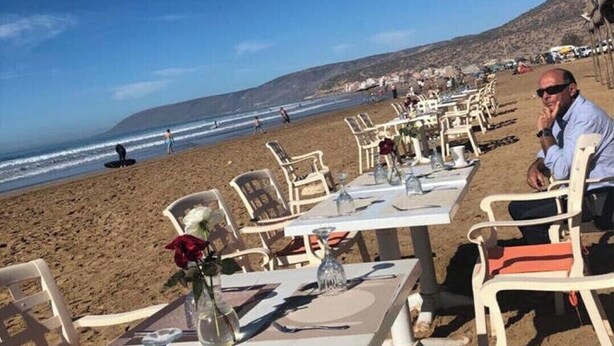 Mobiliario de comedor junto a la playa, con mesas y sillas, con vista al océano.