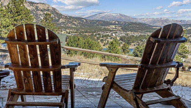 Zwei hölzerne Adirondack-Stühle mit Blick auf eine Berglandschaft und eine Stadt.