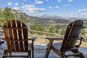 Deux fauteuils Adirondack en bois, placés face à un paysage pittoresque comprenant des montagnes et une ville.