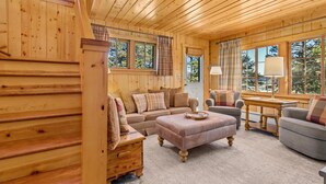 Ein gemütliches Blockhaus-Interieur mit einer Couch, einem Sessel, einem Hocker und einem kleinen Tisch mit einer Lampe.