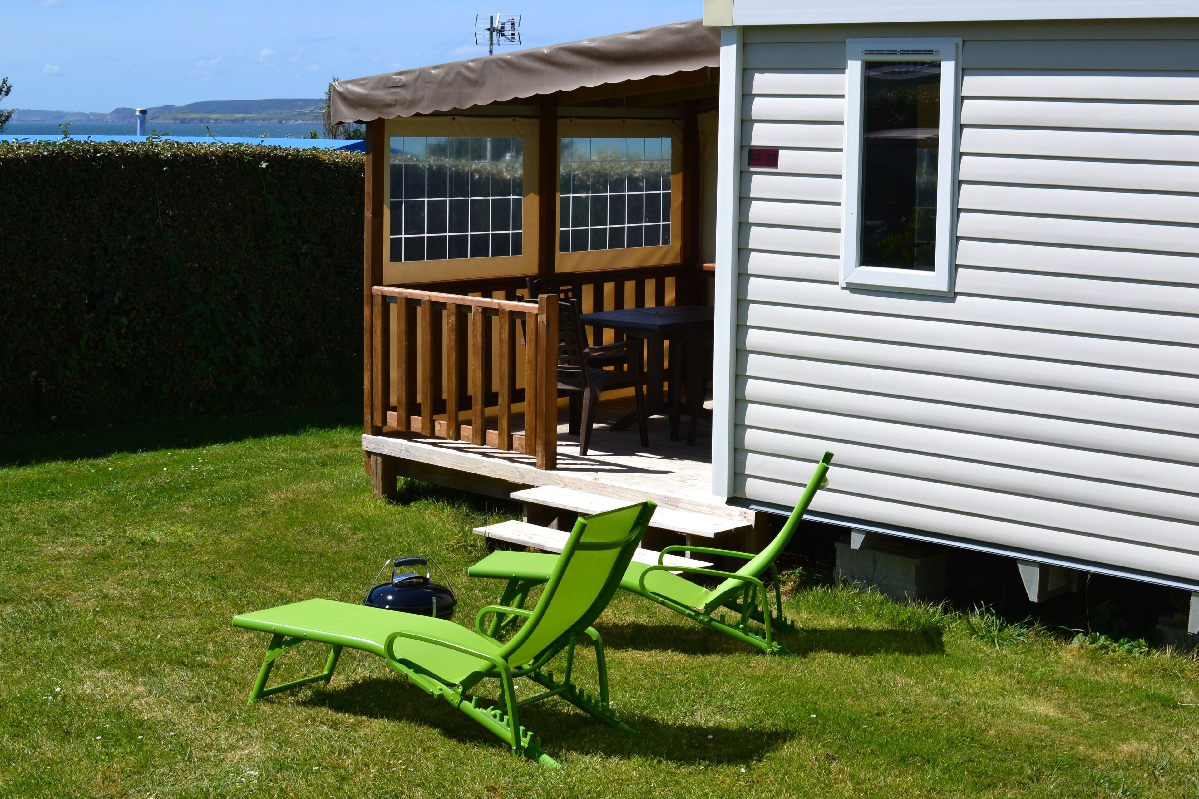 A small house with a porch, a table, and two green lawn chairs.