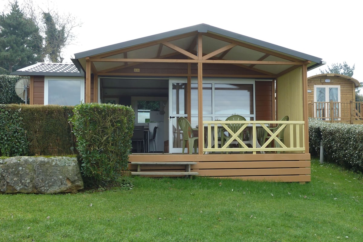 A small wooden cabin with a covered porch, a sliding glass door, and a fenced outdoor seating area.