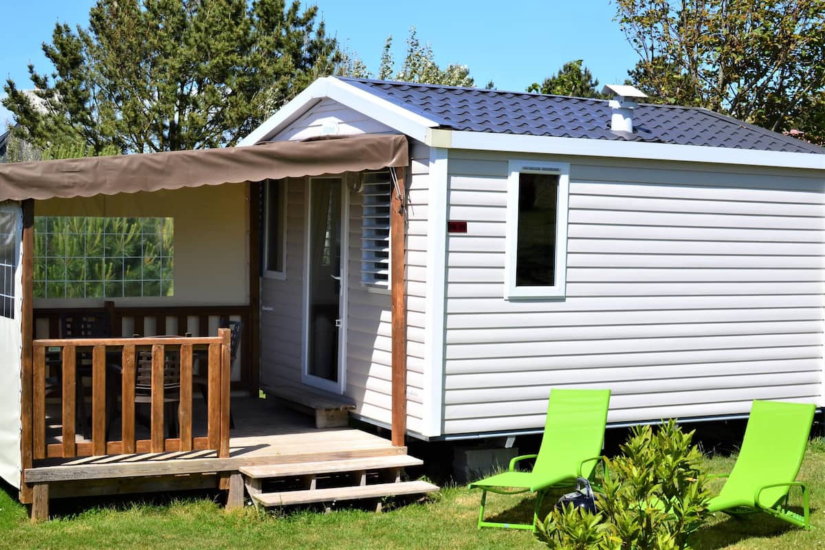 A mobile home with a porch, a small deck, and two green lawn chairs.