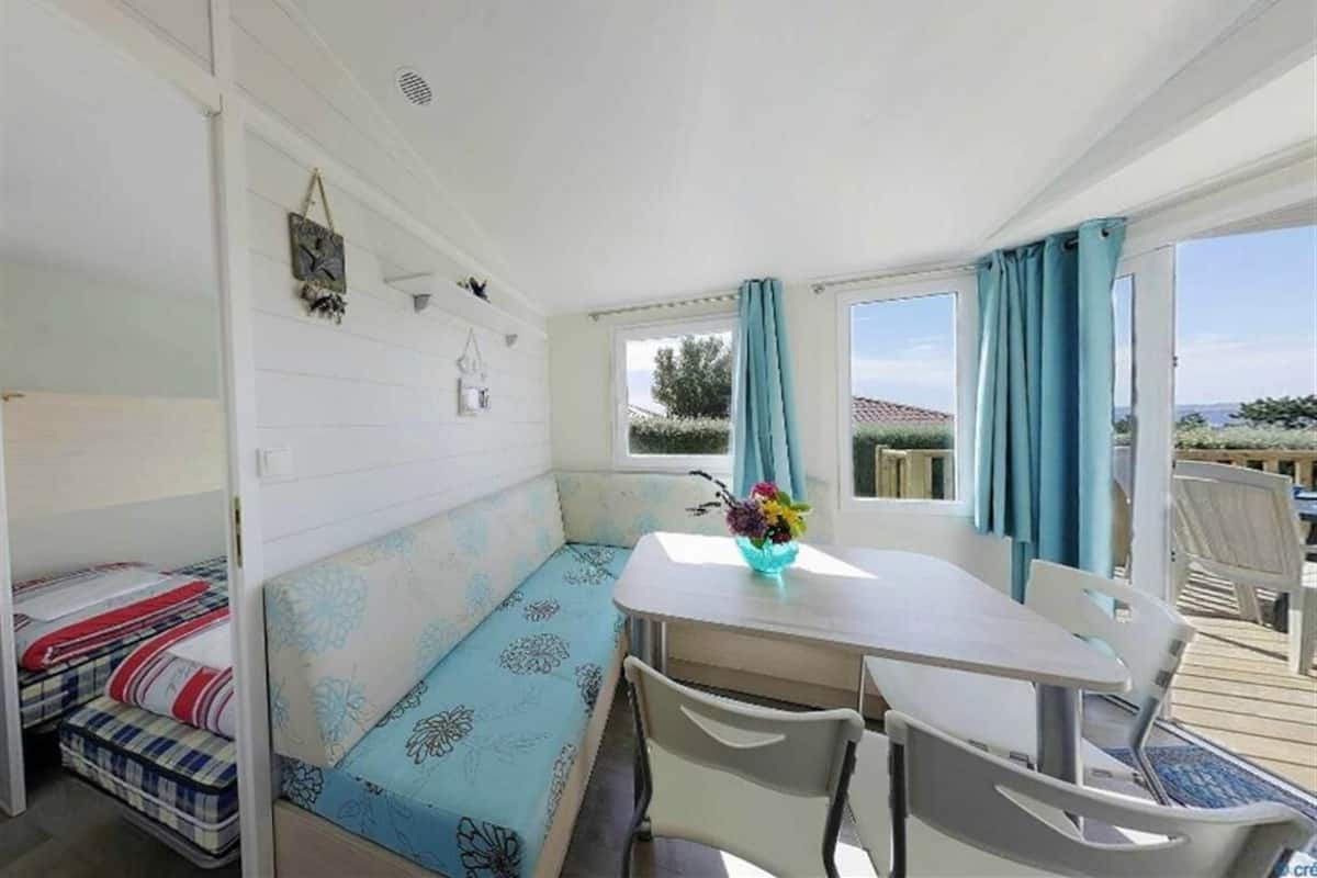 A room with a bed, a table with chairs, a window with curtains, and a view of the outdoors.