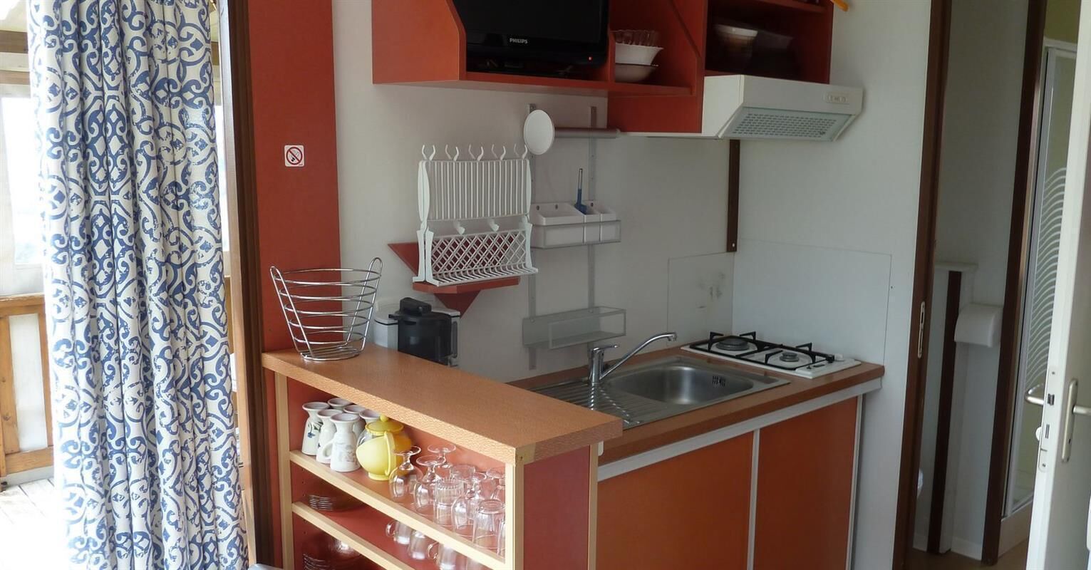 A compact kitchen with a gas stove, sink, and shelves holding kitchenware.