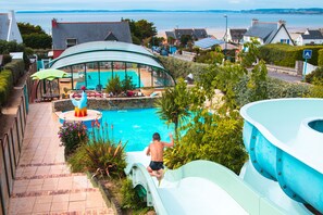 A pool area with a slide, surrounded by greenery and houses.
