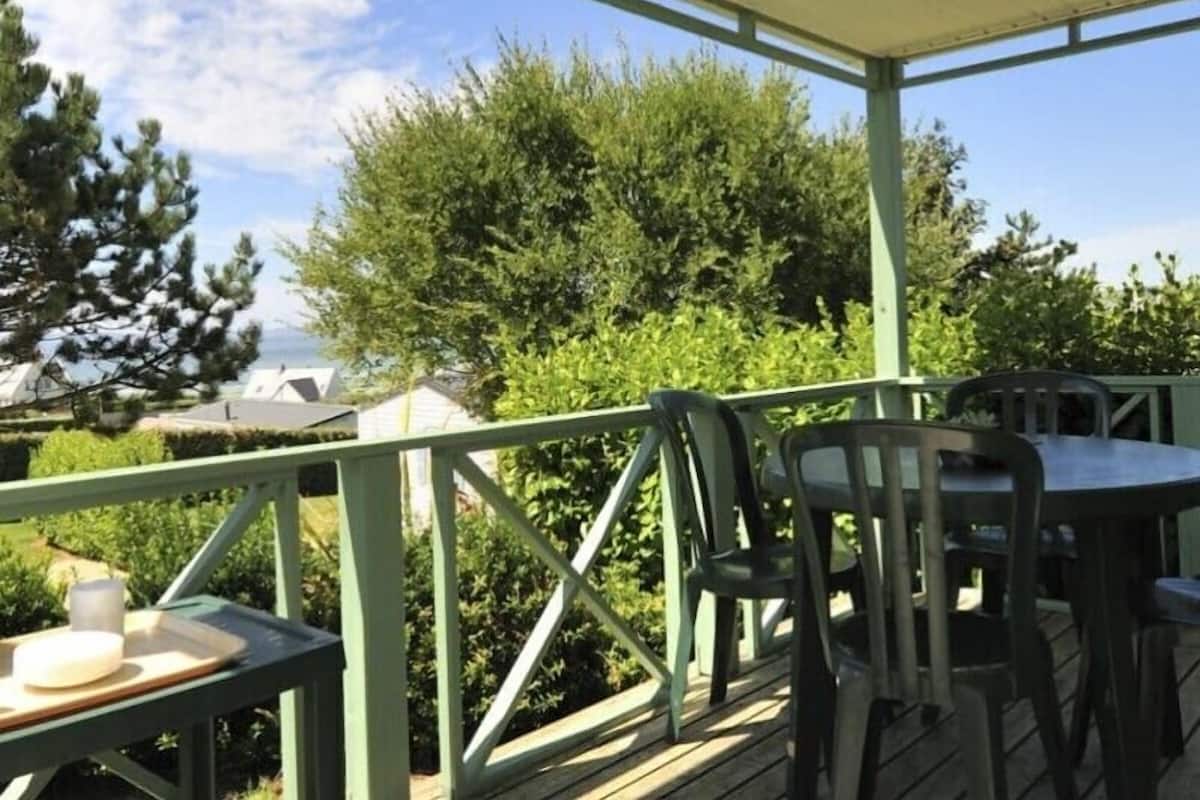 An outdoor patio with a table and chairs, surrounded by greenery and trees.