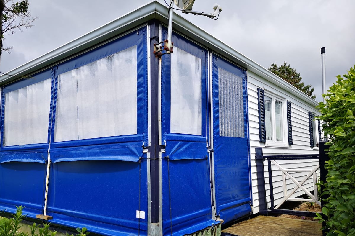 A blue and white mobile home with a wooden deck and a small garden area.