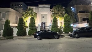 Un edificio con entrada porticada, dos coches aparcados y una fachada bien iluminada de noche.