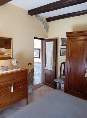 Una habitación con un aparador de madera, un espejo y un cuadro en la pared. Hay una puerta con cortina y una silla en la esquina.