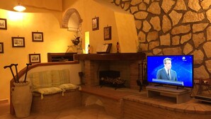 A cozy living room with a stone wall, fireplace, and a television displaying a news channel. - Ancient village of the well "Casa La Corte" (Tramonti (SA))