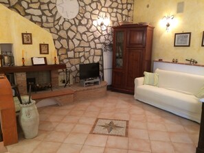 Una sala de estar con pared de piedra, chimenea, televisor, mueble y sofá blanco.