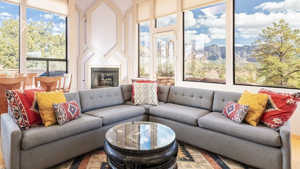 A modern living room with a sectional sofa, a glass coffee table, and large windows offering a view of the outdoors. - Experience luxury in Sedona Painted Sky—sleeps 8 with stunning panoramic views. (Sedona)