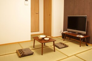 Una habitación japonesa tradicional con suelo de tatami, una mesa baja con cuencos, un televisor sobre un pedestal y una puerta corredera.