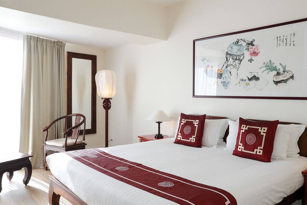 A hotel room with a large bed, a chair, a bedside table, a lamp, and a wall with a framed artwork.