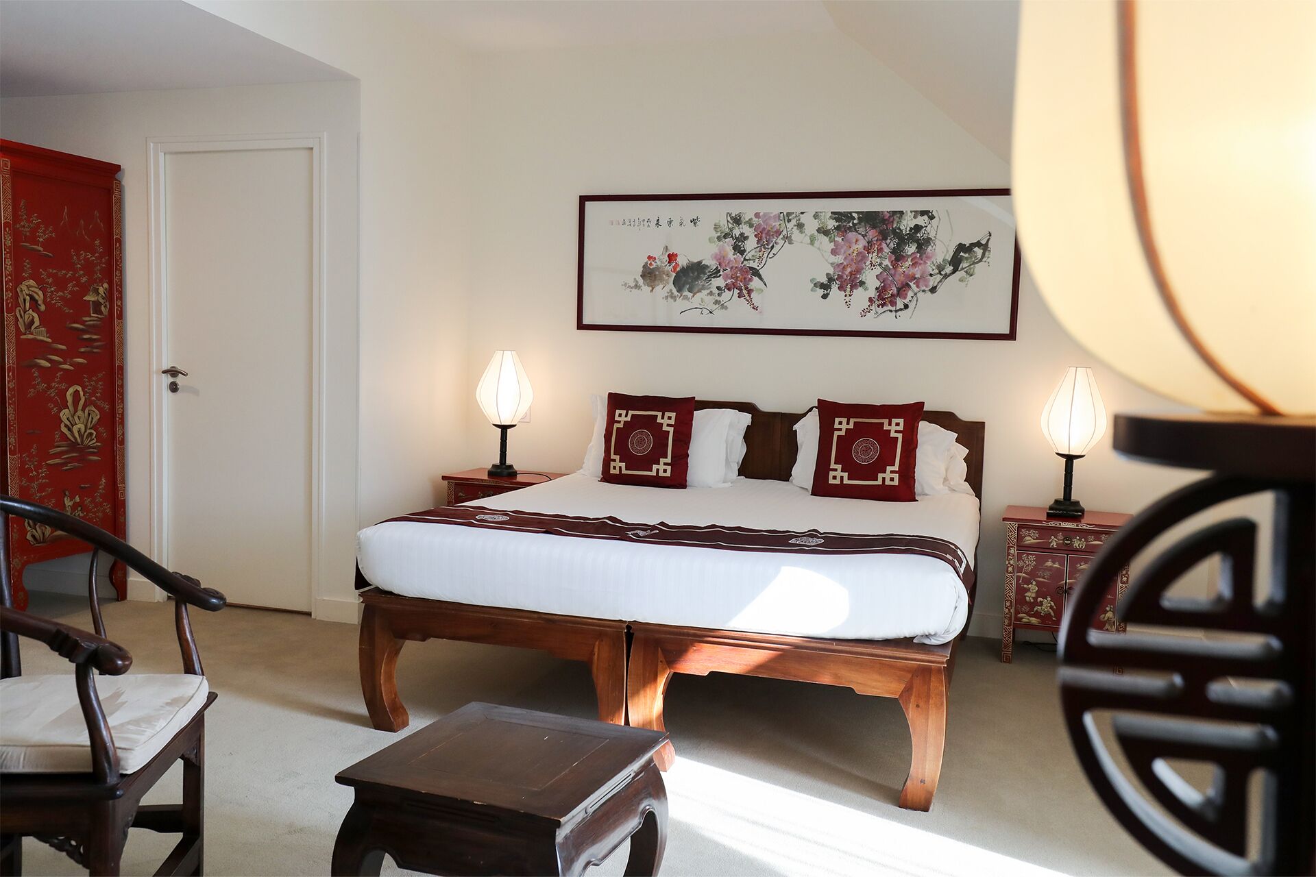 Habitación de hotel ordenada con una cama grande, dos mesitas de noche con lámparas, una silla y una pequeña mesa.