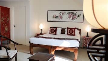 Habitación de hotel ordenada con una cama grande, dos mesitas de noche con lámparas, una silla y una pequeña mesa.