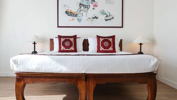 A neatly made bed with white linens, two red pillows with intricate designs, and a wooden bench at the foot of the bed.