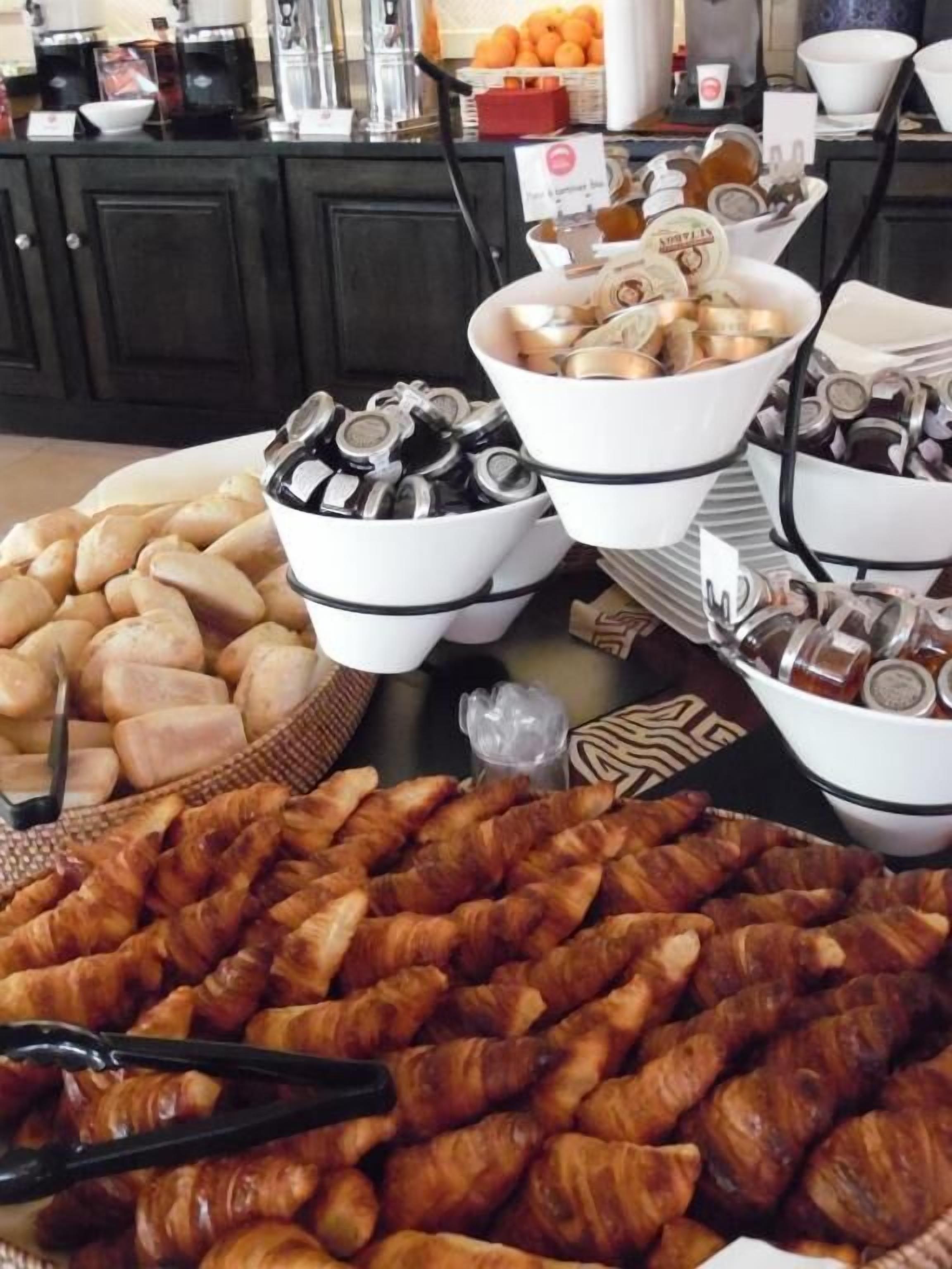 Une table de buffet proposant une variété d’aliments, notamment du pain, des pâtisseries et des condiments.