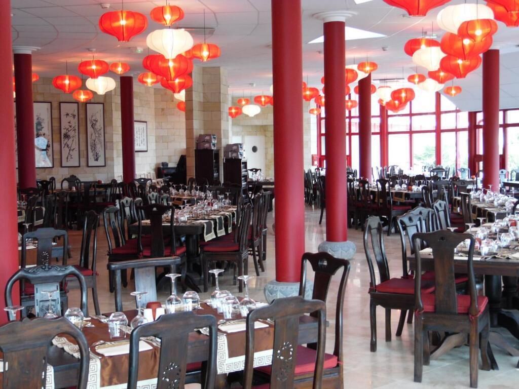 Un restaurante con varias mesas y sillas, pilares rojos y faroles rojos colgantes.