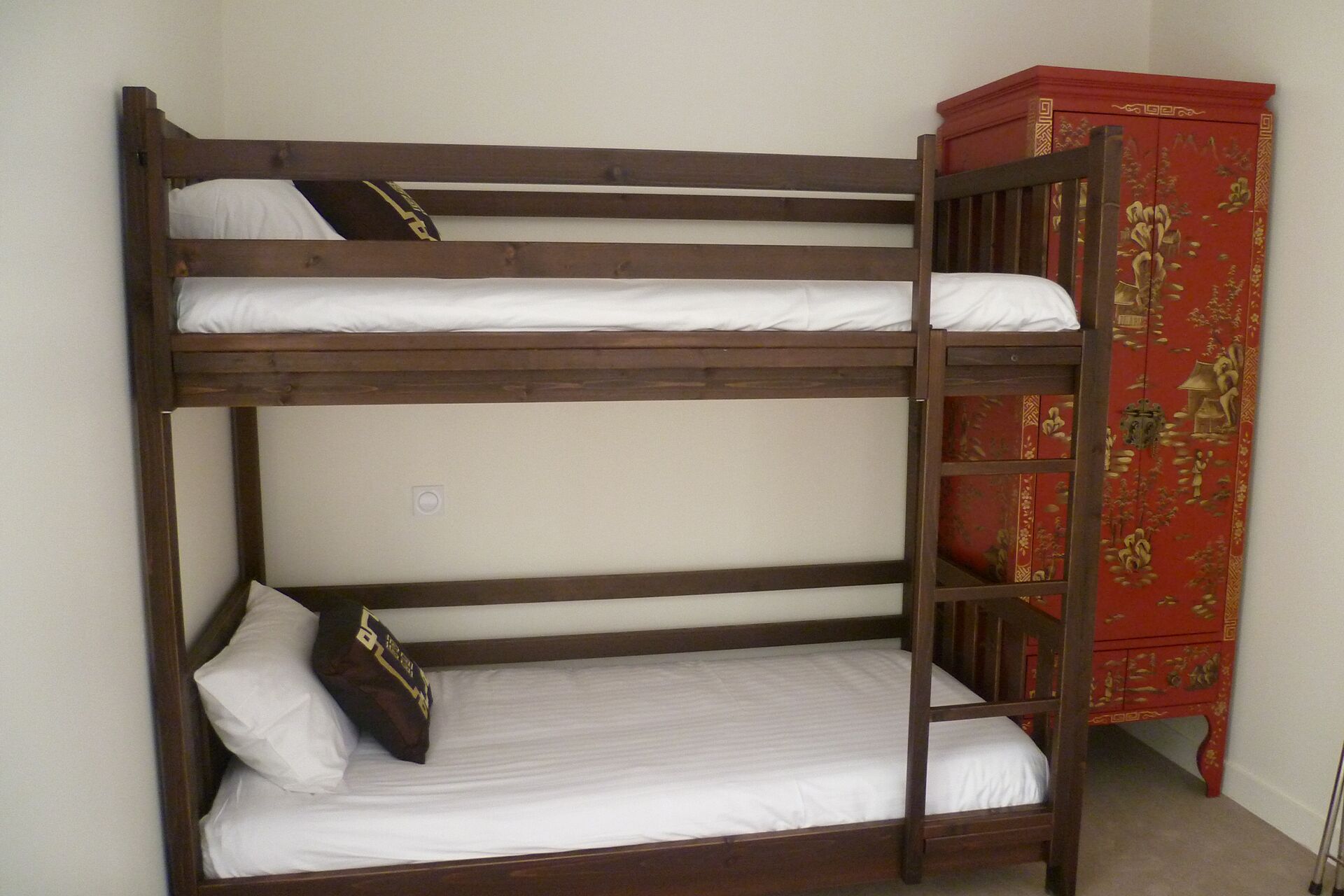 Un lit superposé avec une literie blanche et une armoire rouge ornée de motifs décoratifs.