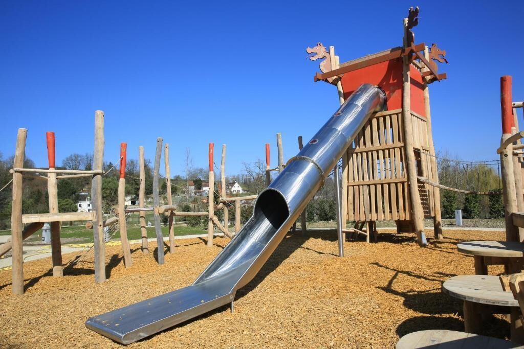 A playground with a metal slide, wooden climbing structures, and a red playhouse.
