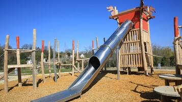 A playground with a metal slide, wooden climbing structures, and a red playhouse.