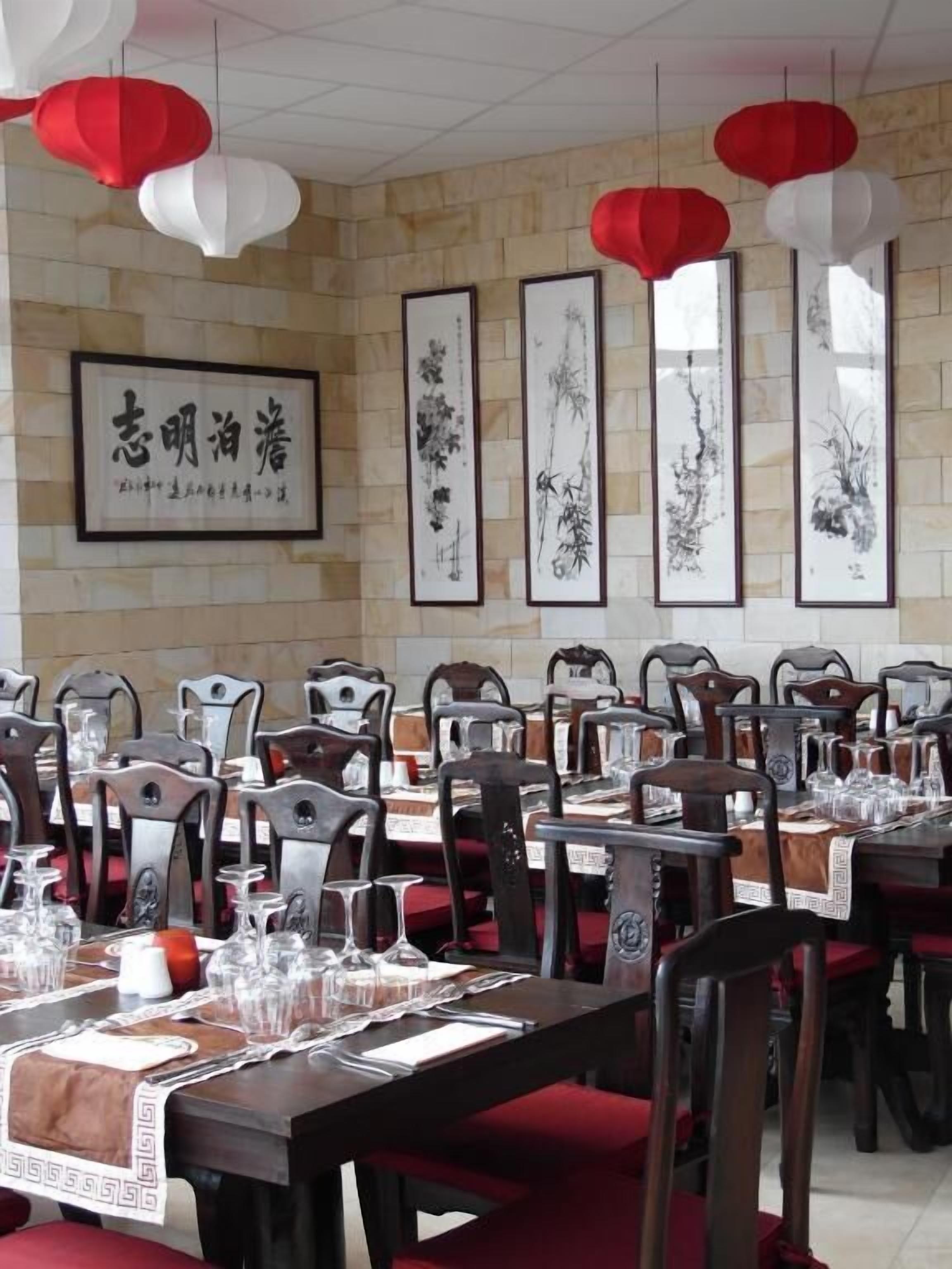 A dining area with tables set for service, framed artwork on the wall, and red and white hanging decorations.