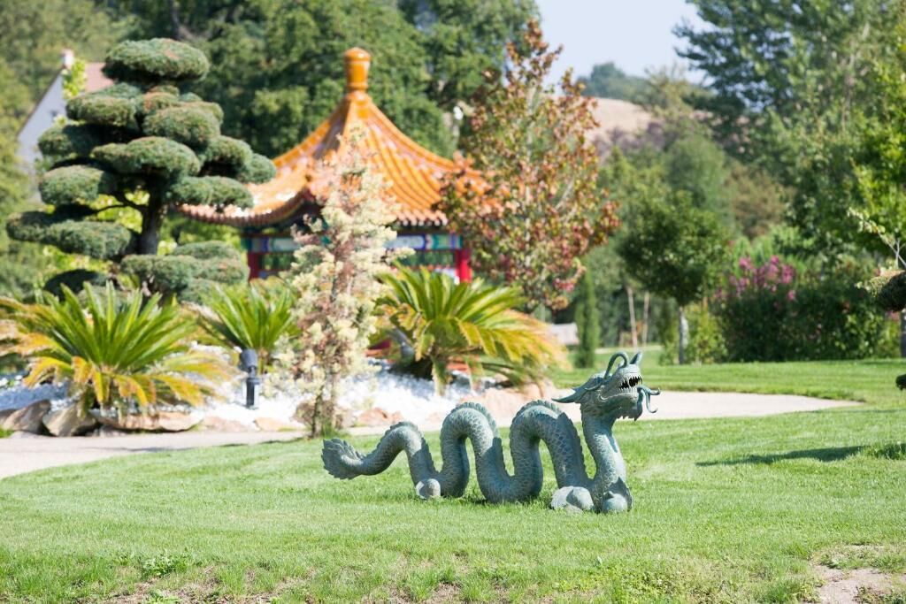 A dragon statue in a park with a traditional building in the background.