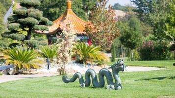 A dragon statue in a park with a traditional building in the background.