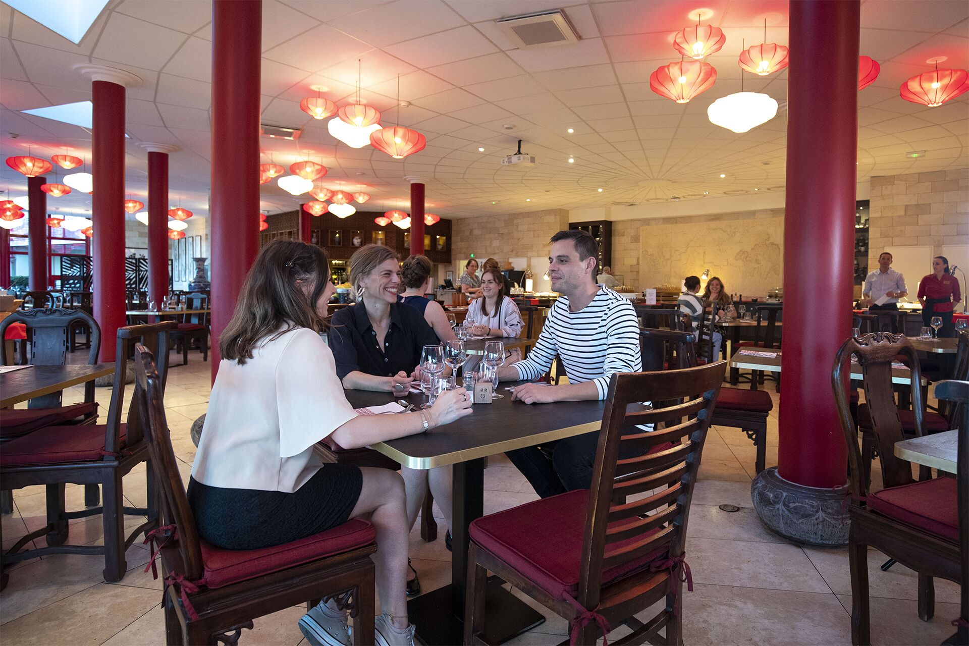 En restaurang med träbord och stolar, röda pelare och hängande röda lyktor.