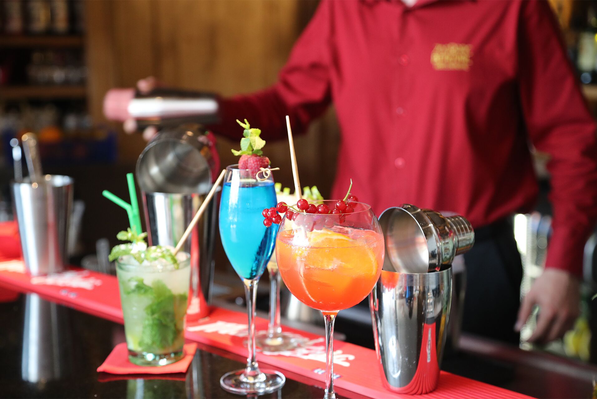 Un bar avec trois cocktails, un shaker et un barman portant une chemise rouge.