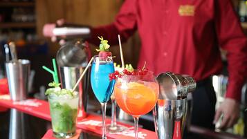 Un bar avec trois cocktails, un shaker et un barman portant une chemise rouge.