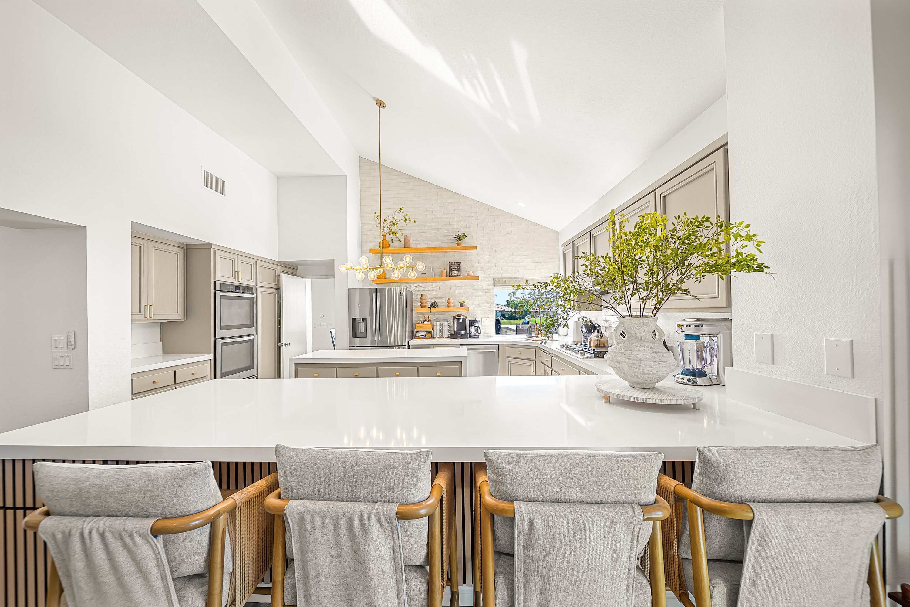 A modern kitchen with a large island, bar stools, and a hanging light fixture.