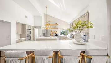 A modern kitchen with a large island, bar stools, and a hanging light fixture.