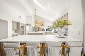 Une cuisine moderne dotée d’un grand îlot central, de tabourets de bar et d’un luminaire suspendu.