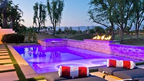 An outdoor swimming pool with a fire feature, surrounded by lounge chairs and a landscaped garden. - Casa Havana  Stunning Views Pool Spa PGA West 4br (La Quinta)