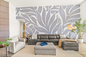A living room with a sectional sofa, a grey ottoman, a small side table, and a potted plant. - Casa Havana  Stunning Views Pool Spa PGA West 4br (La Quinta)