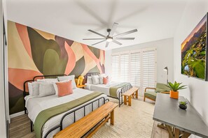 A modern bedroom with a large abstract wall mural, a ceiling fan, a bed with a bench, a small table, and a TV on the wall.