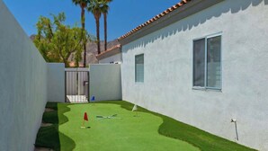 A small, enclosed backyard with artificial green turf, a red flag, and a golf club. - Casa Havana  Stunning Views Pool Spa PGA West 4br (La Quinta)