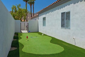 A small, enclosed backyard with artificial green turf, a red flag, and a golf club. - Casa Havana  Stunning Views Pool Spa PGA West 4br (La Quinta)