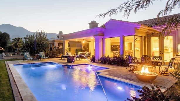 A swimming pool with a water feature, outdoor seating, and a fire pit.