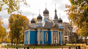 Una iglesia azul con múltiples cúpulas y cruces, rodeada de árboles y bancos en un parque.