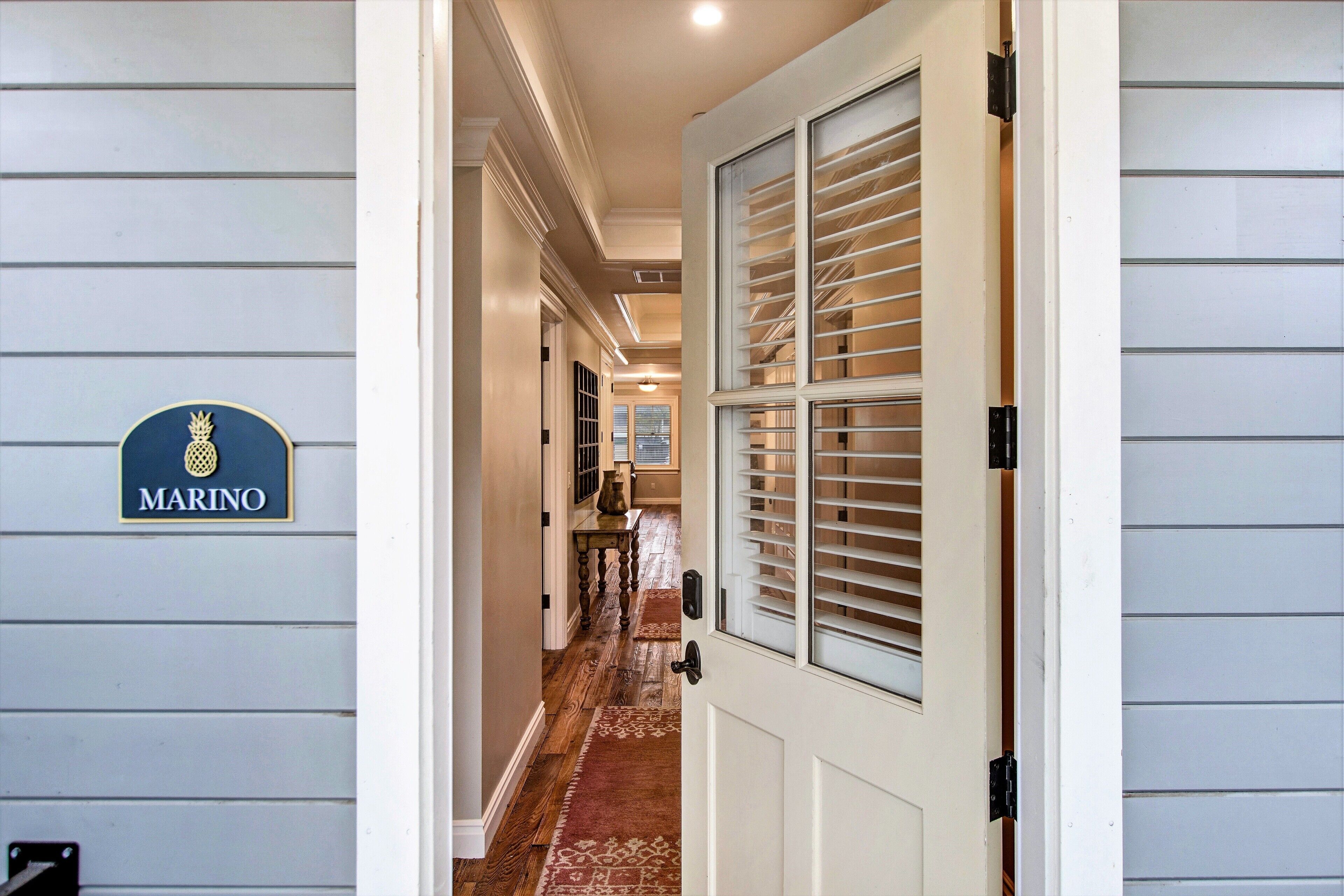 A hallway with a 'MARINO' sign, wooden flooring, a patterned rug, and a door with blinds.