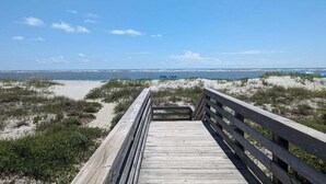 A wooden boardwalk leading to a beach with sand dunes and sparse vegetation.