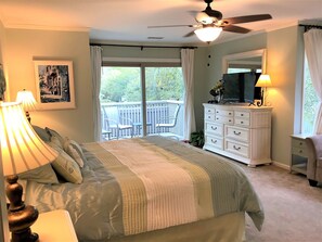 A bedroom with a bed, a dresser, a ceiling fan, a TV, and a balcony with chairs.