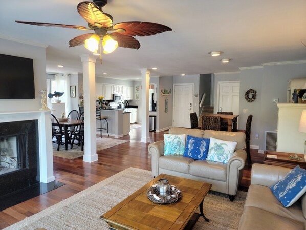 A spacious living room with a fireplace, a ceiling fan, and a dining area in the background.